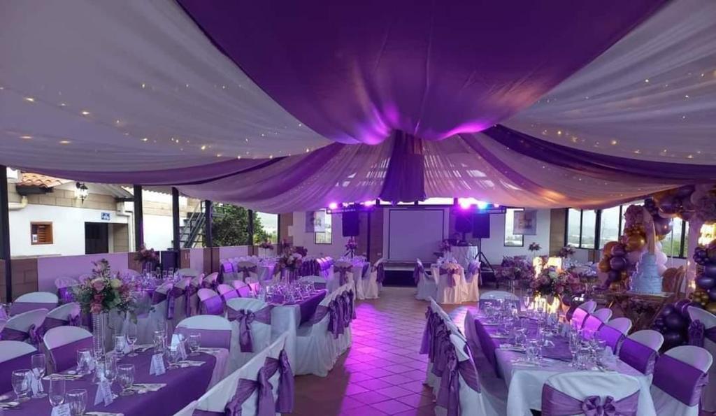 une salle de banquet avec des tables blanches et des plafonds violets dans l'établissement La Martina Campestre, à Sutamarchán