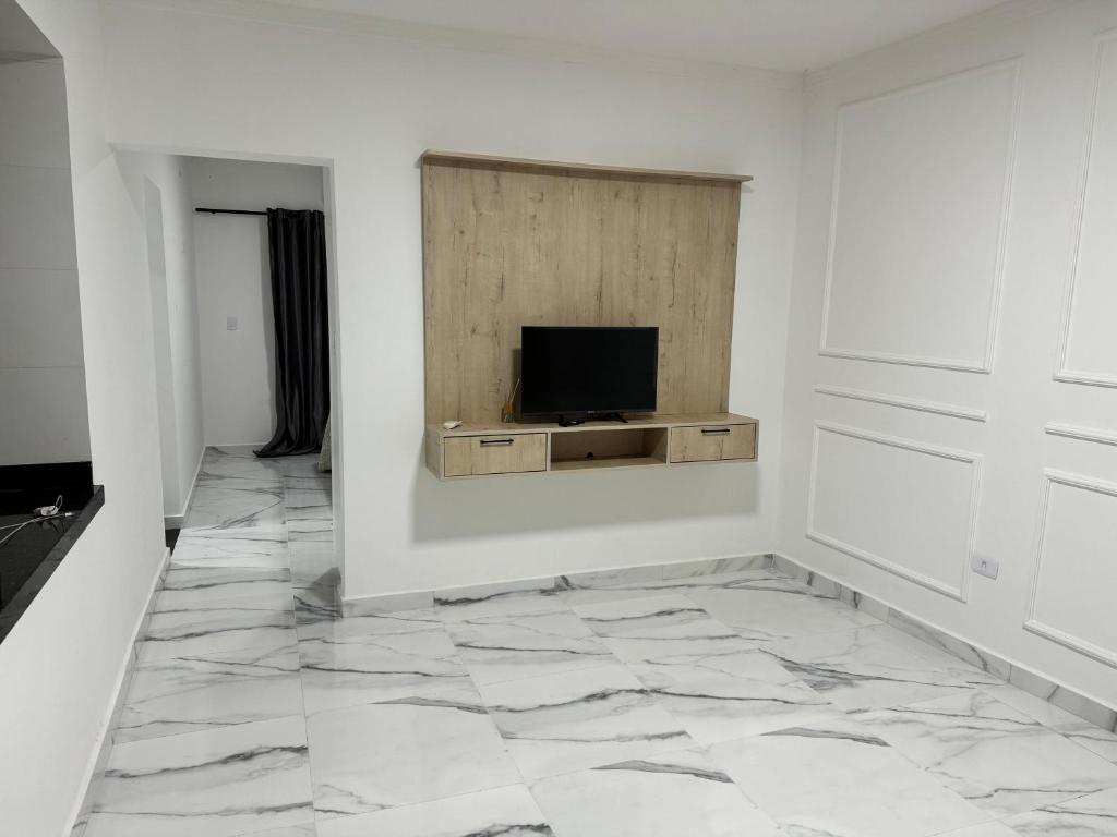 un salon avec une télévision sur un mur blanc dans l'établissement Villa Serenità, à Peruíbe