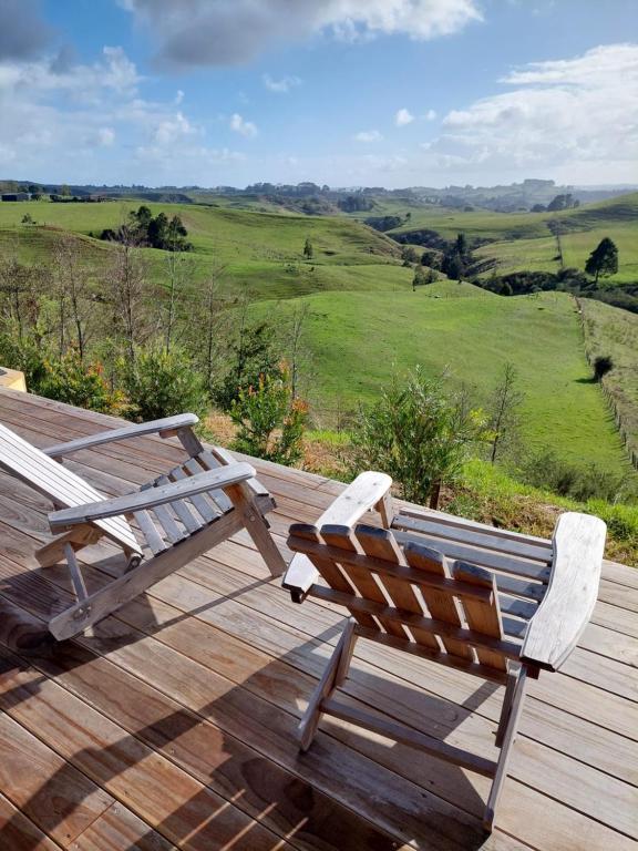 a wooden deck with two chairs and a view of a field at Onewhero Country Cabin in Onewhero