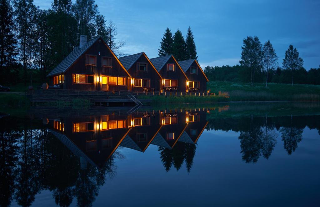 une maison sur un lac la nuit avec ses lumières allumées dans l'établissement Kivi Talu Country Hotel, à Otepää