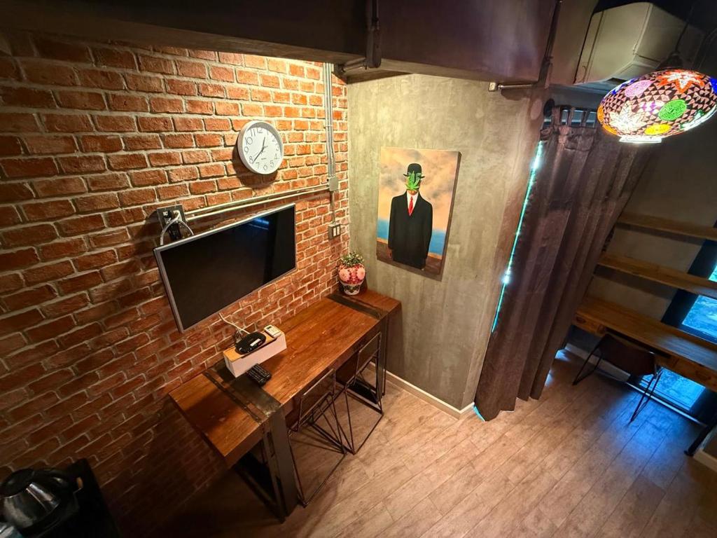 A compact desk sits beneath a wall-mounted television beside a brick feature wall and stairway.
