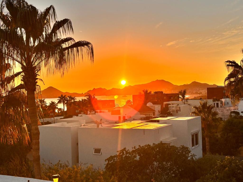einen Sonnenuntergang über einem weißen Gebäude mit einer Palme in der Unterkunft Spectacular Vacation Home Ocean View Walk to Beach in Cabo San Lucas