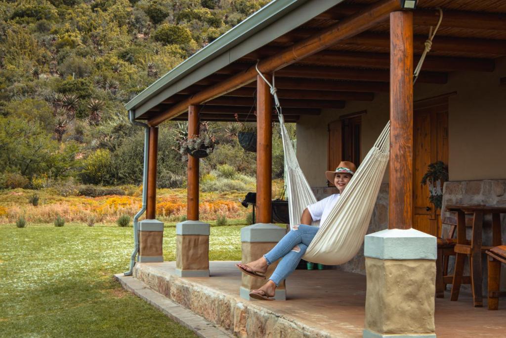 una donna seduta su un portico su un'amaca di Vogelsang Farm Cottage a Oudtshoorn