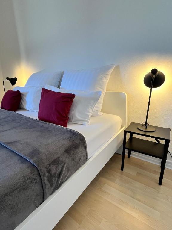a white bed with red pillows and a lamp on a table at Zentrumsnahe Wohnung, Anviolhomes in Hannover