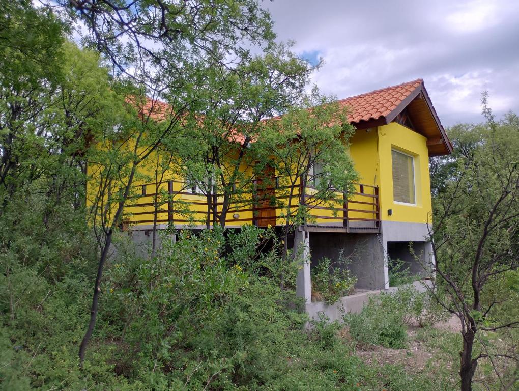 a yellow house on top of a hill with trees at Secretos del quebracho in Capilla del Monte
