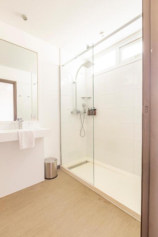 a bathroom with a glass shower and a sink at Hotel Beaurivage in Noumea
