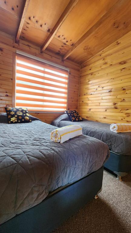 2 Betten in einem Blockhaus mit Fenster in der Unterkunft Cabaña kiro in Dalcahue