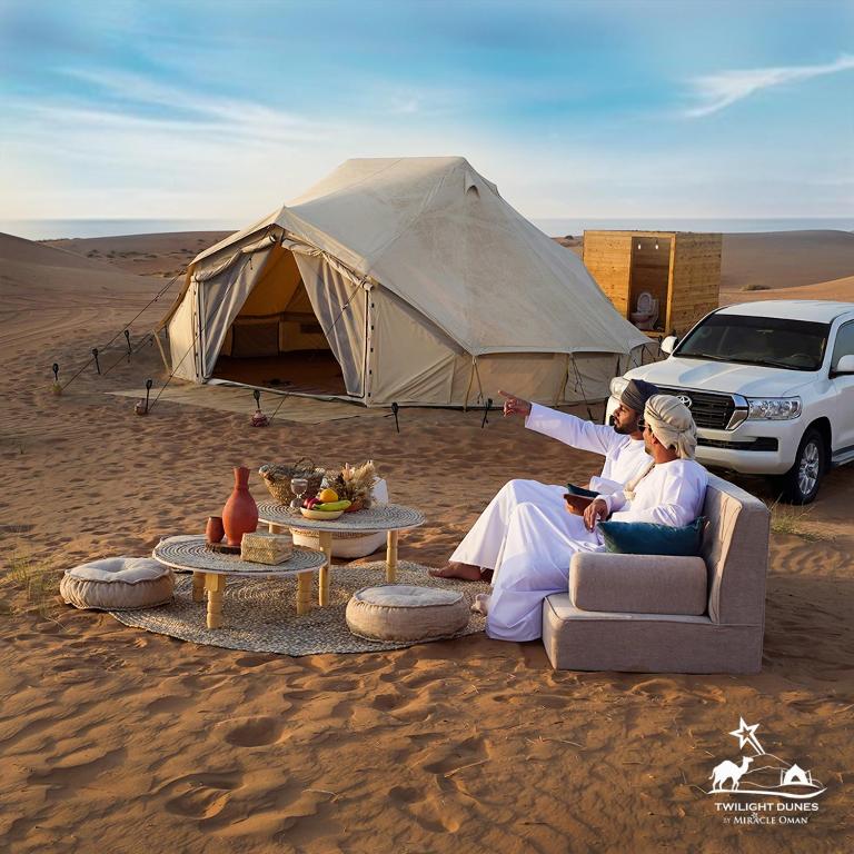 a couple sitting in front of a tent in the desert at Twilight Dunes by Miracle Oman in Badīyah