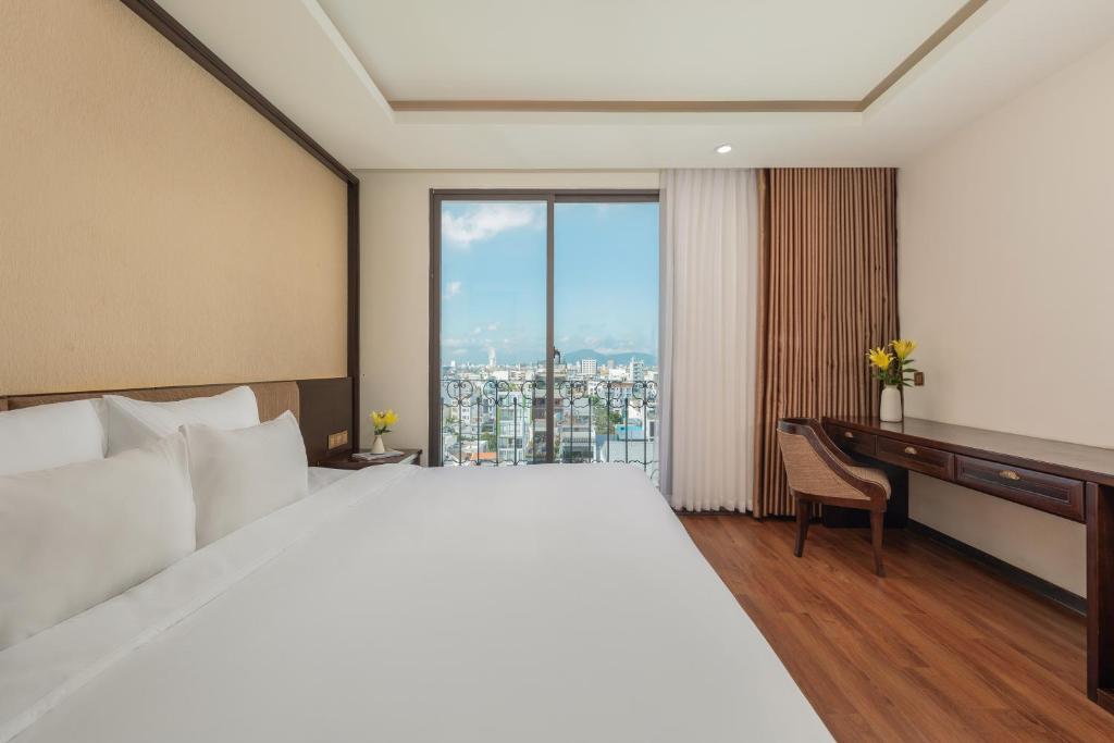 A bright bedroom with a large bed, compact desk and city-and-water view.