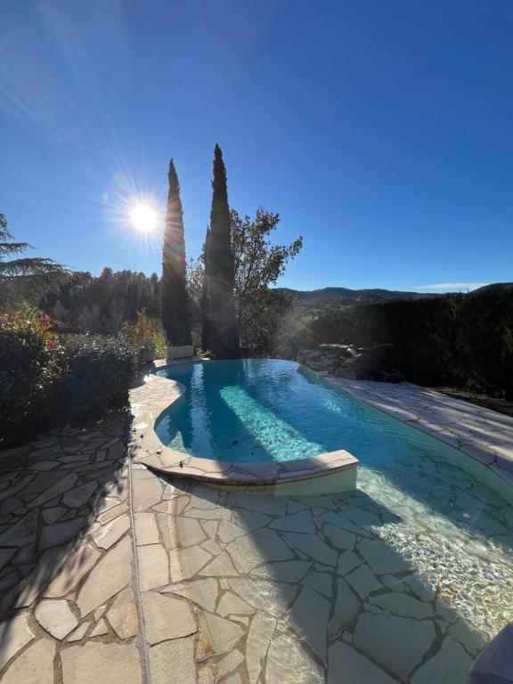 - une piscine avec des arbres et le soleil dans le ciel dans l'établissement Sous le Soleil des Adrets, à Montauroux