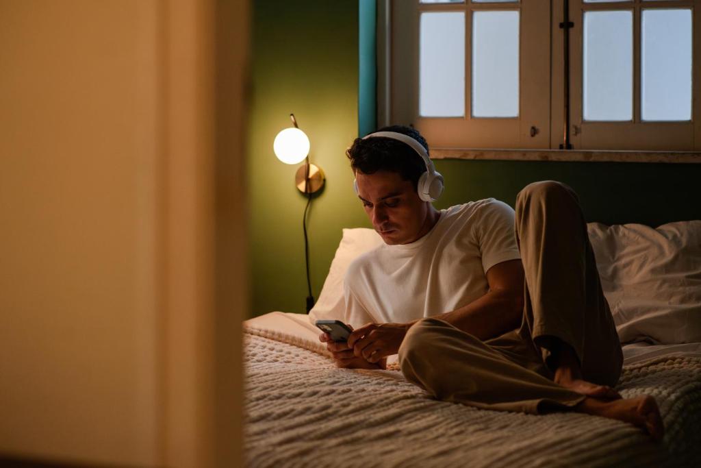 a man sitting on a bed looking at a cell phone at Chez Zany Boutique Hostel - Copacabana in Rio de Janeiro