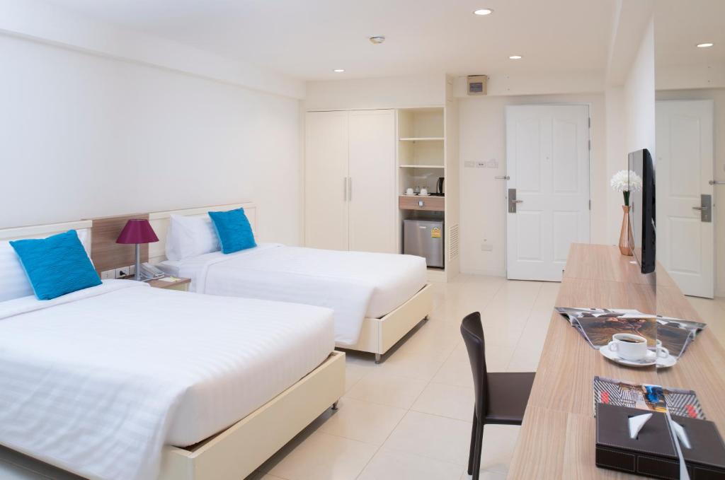 A twin room with a long desk, dining-style chair, television, and in-room beverage setup.
