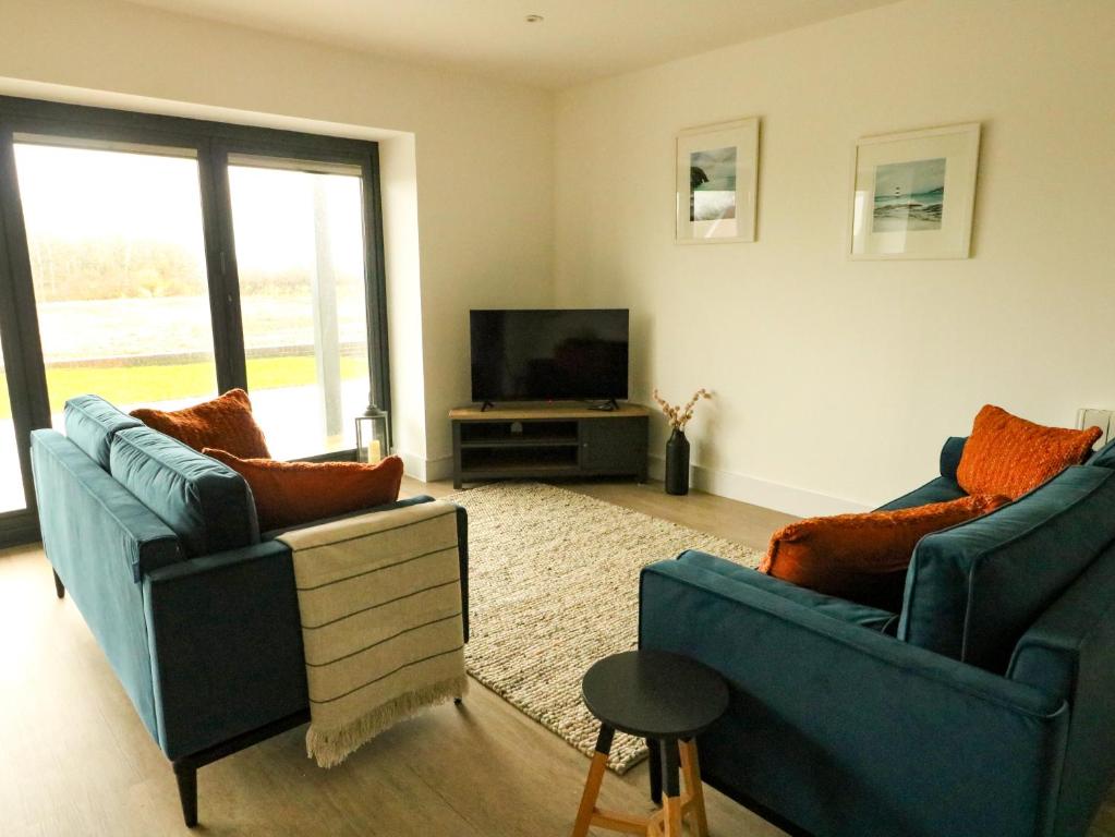 a living room with two blue chairs and a television at Glynllifon 2 in Llanallgo