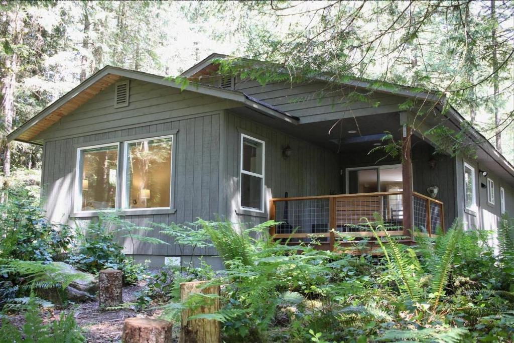 a small gray house with a porch in the woods at Glacier Springs Cabin - Wood Stove, Hot Tub, WIFI, Sleeps 8 in Deming