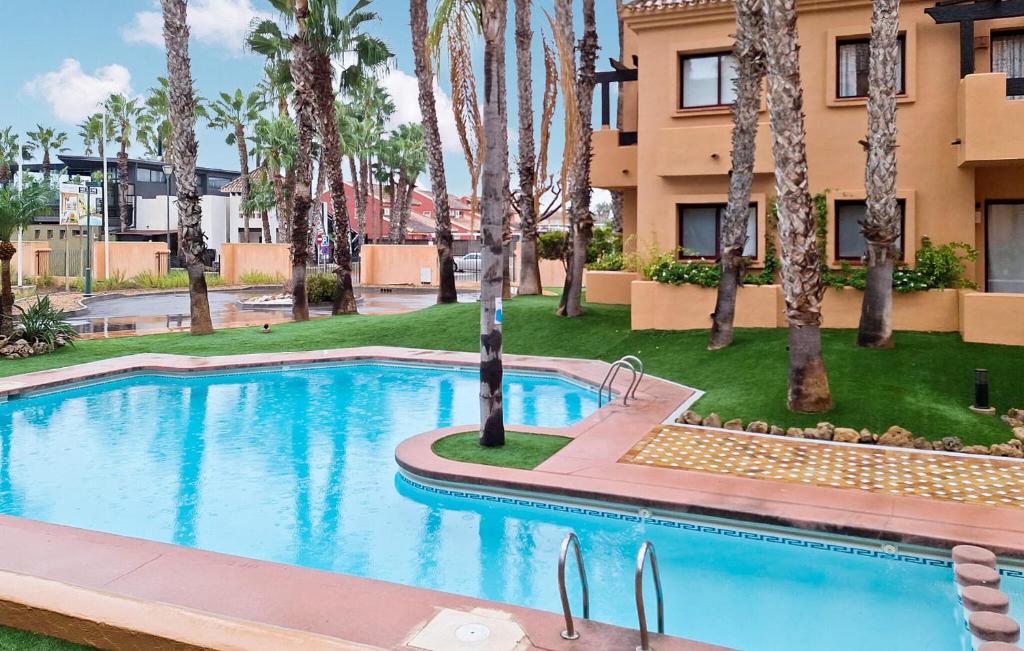 a swimming pool in front of a building with palm trees at Beautiful Apartment In Los Alcazares in Los Alcázares