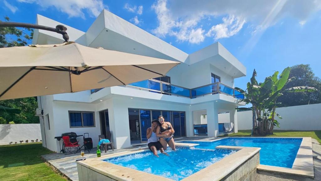 deux personnes debout dans une piscine devant une maison dans l'établissement VillaGuerra-Piscina-Billar-BBQ-WiFi-Cozy-3Br-5Bds-7Pax, à Guerra