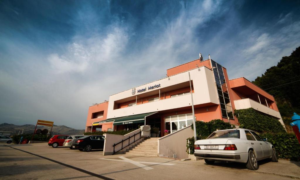 un bâtiment avec des voitures garées dans un parking dans l'établissement Hotel Merlot, à Opuzen