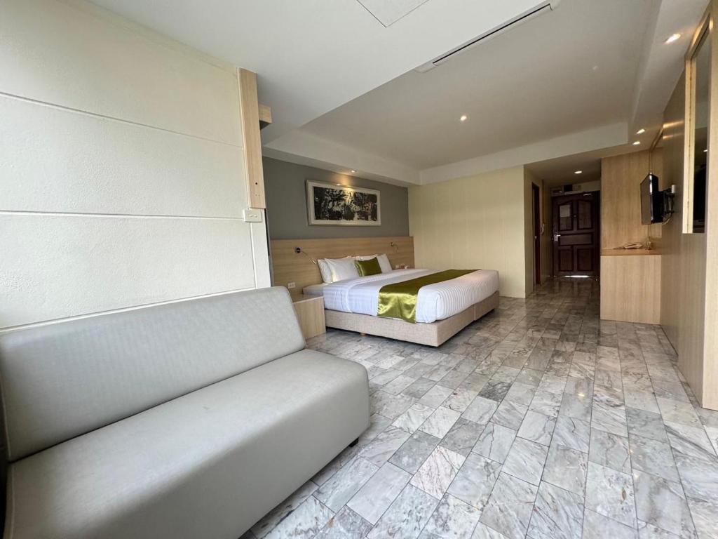 A wide room view showing a large bed, sofa, desk, and tiled floor.