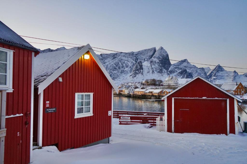 a couple of red buildings with mountains in the background at Anitas Waterfront Cabins in Reine