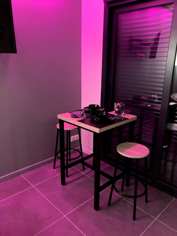 une table avec tabourets dans une pièce à éclairage violet dans l'établissement F2 Ti amo 1 chambre, à Saint-Germain-lès-Corbeil