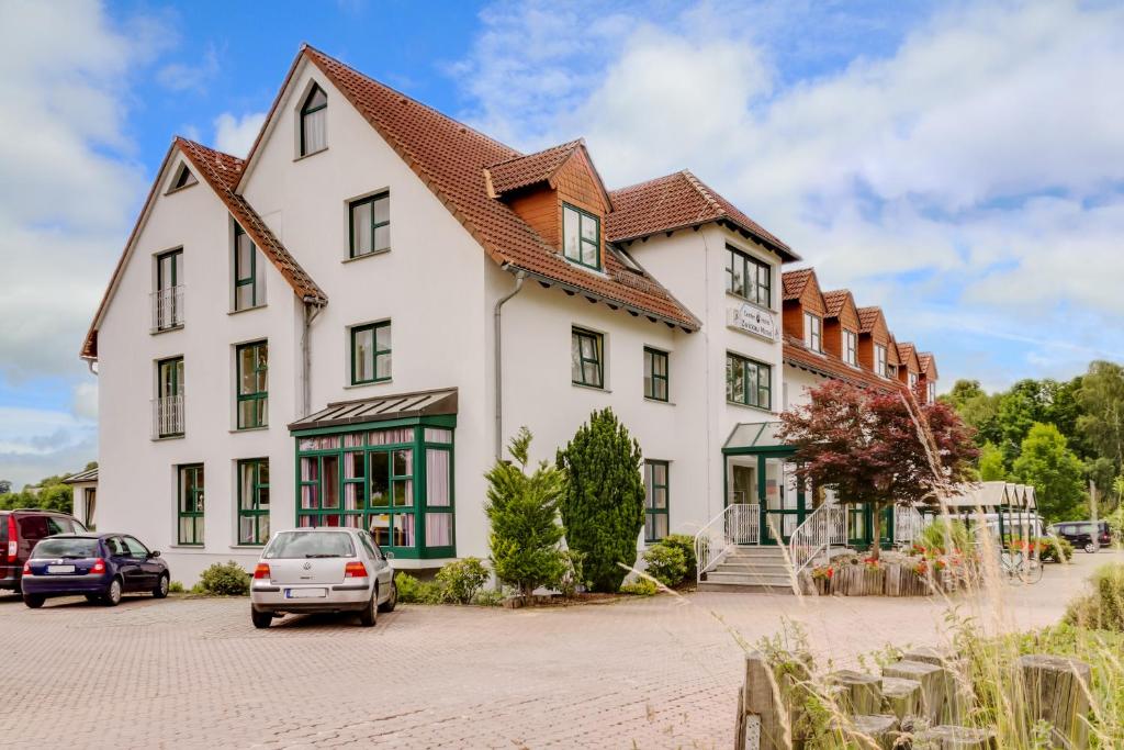 ein großes weißes Gebäude mit Autos auf einem Parkplatz in der Unterkunft Hotel garni Zwickau-Mosel in Mülsen