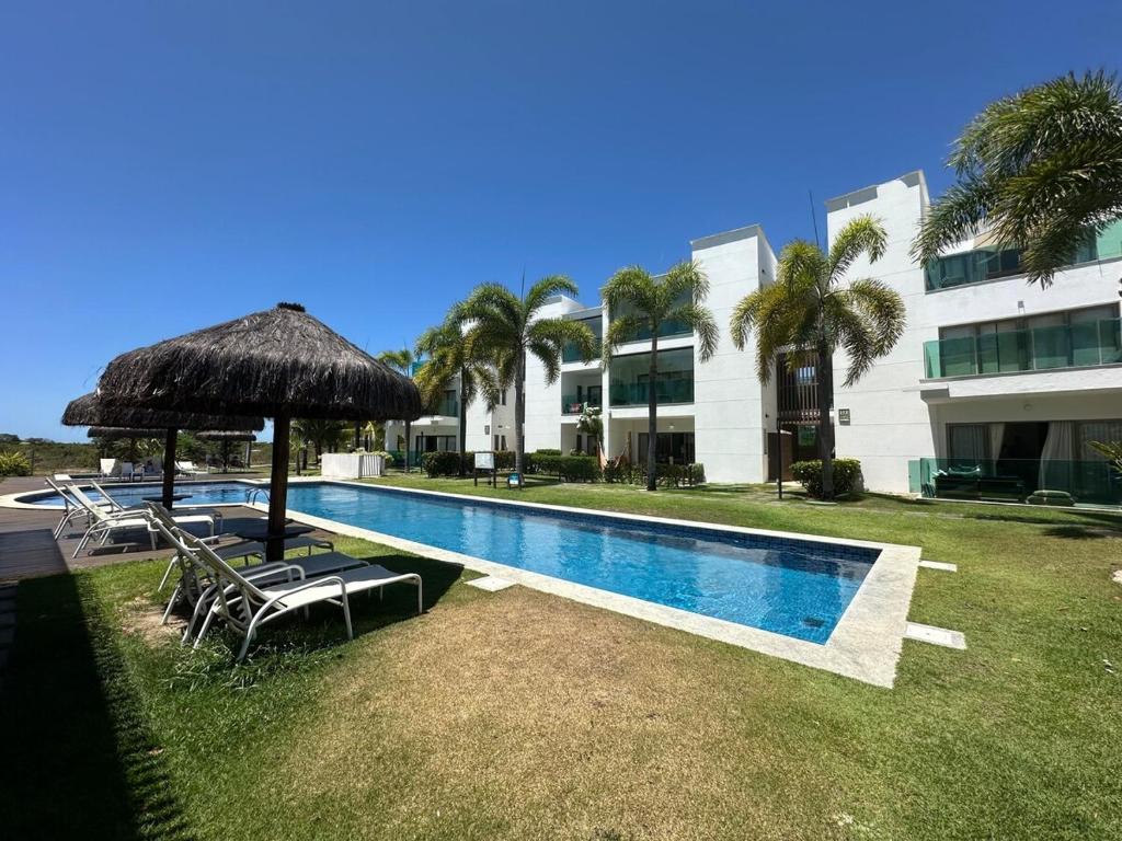 a swimming pool with chairs and an umbrella next to a building at Apartamento Iberostate Praia do Forte, 2 quartos in Mata de Sao Joao