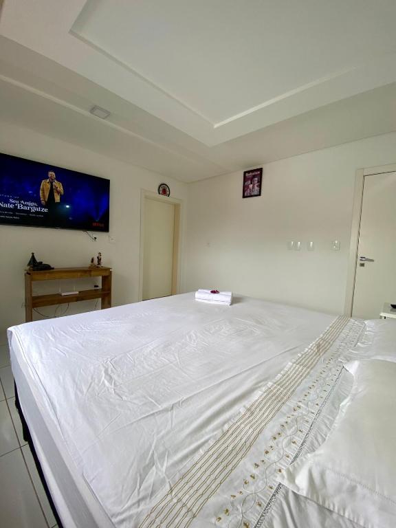 a white bed in a bedroom with a tv on the wall at Casa Ampla na Brava in Itajaí