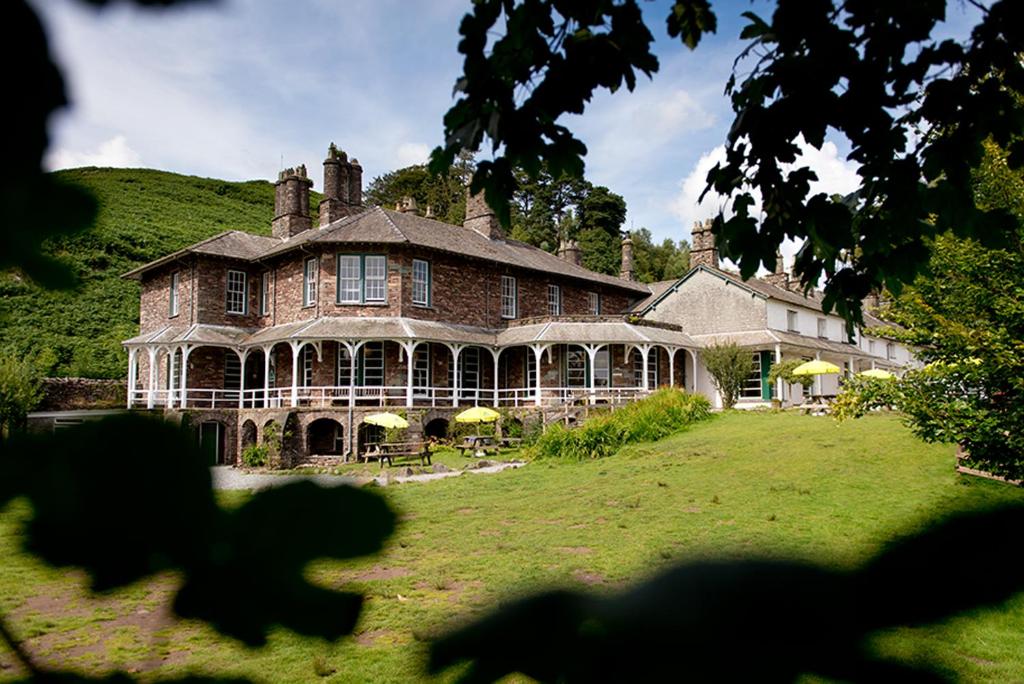 une grande maison en briques avec une colline verdoyante derrière elle dans l'établissement YHA Langdale, à Ambleside