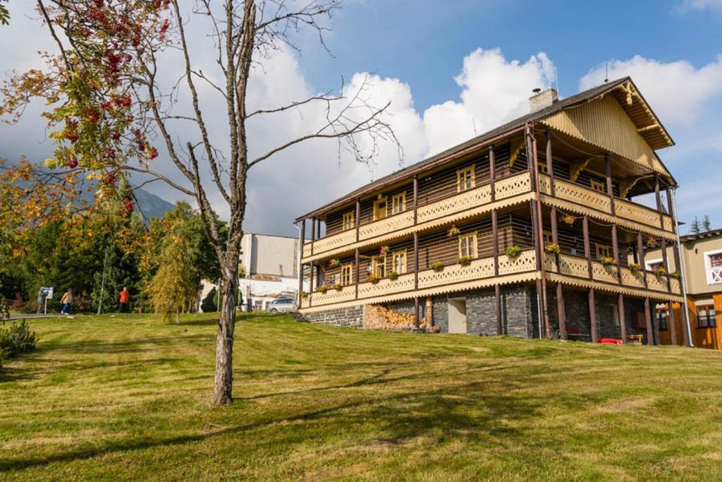 un grand bâtiment en bois sur une colline avec un arbre dans l'établissement Švajčiarsky Dom, à Starý Smokovec