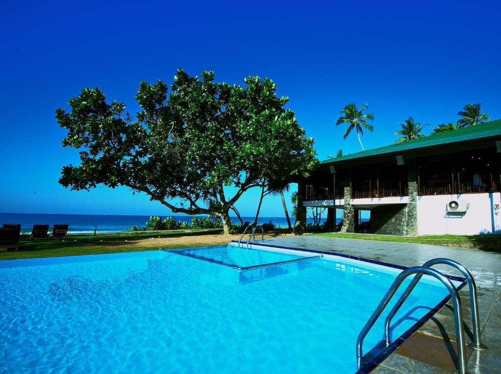 een zwembad met een boom en de oceaan bij Koggala Beach Hotel in Koggala