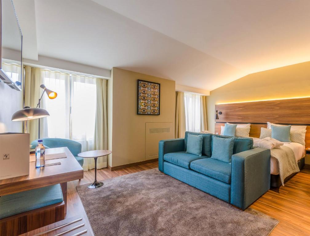 A larger open-plan room with a double bed, blue sofa, desk and two windows.