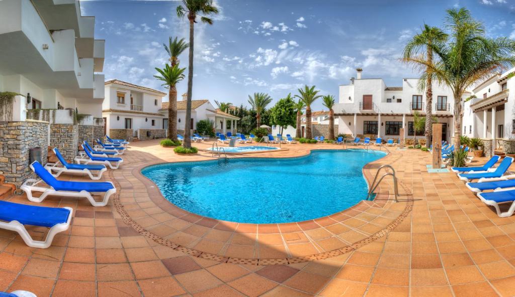 una piscina con sillas azules y palmeras en Hotel Porfirio en Zahara de los Atunes