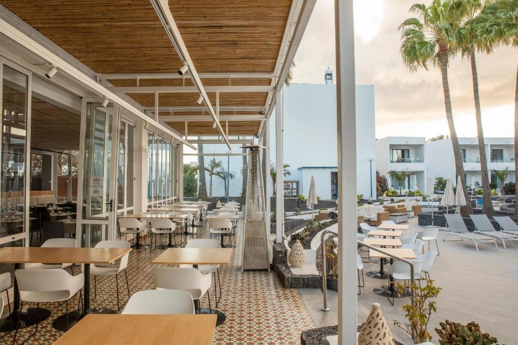 an outdoor patio with tables and chairs and palm trees at Oasis Lanz Beach Mate in Costa Teguise