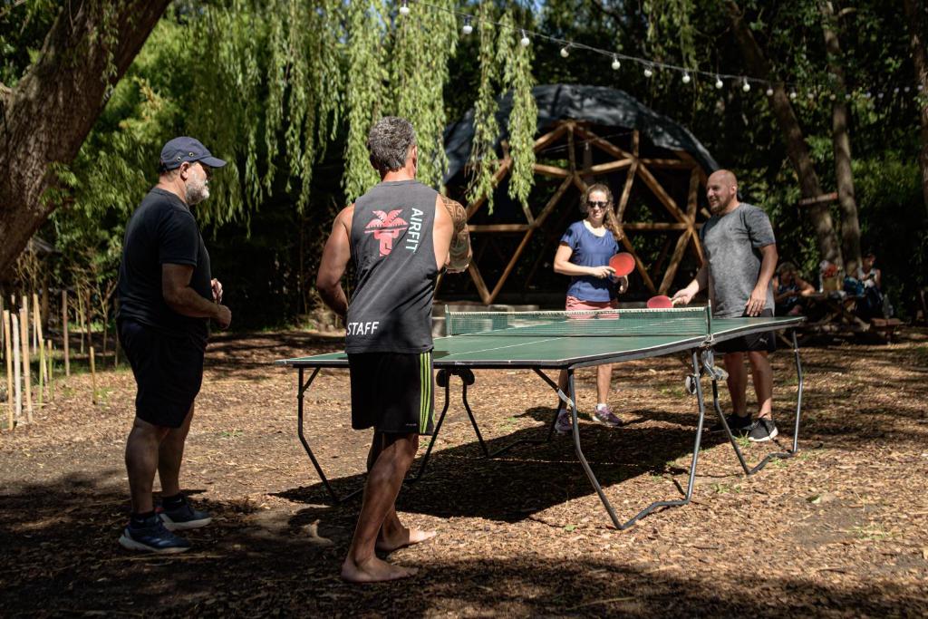 Un grupo de personas de pie alrededor de una mesa de ping pong. en HOSTEL CASA C Alojamiento, Coworking y Centro Cultural, en Villa General Belgrano