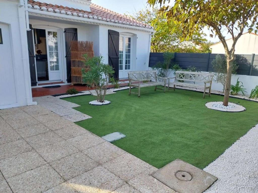 une arrière-cour avec une pelouse verte et deux bancs dans l'établissement Le Bananier, à Les Sables-dʼOlonne