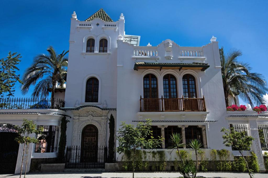 a white house with a balcony and palm trees at Hotel Boutique Cultura Manor by Brater in Quito