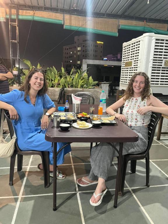 two women sitting at a table with food on it at Paarijat PG in Udaipur