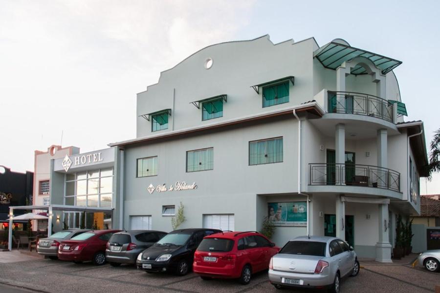 ein weißes Gebäude mit Autos auf einem Parkplatz in der Unterkunft Hotel Villa de Holanda in Holambra