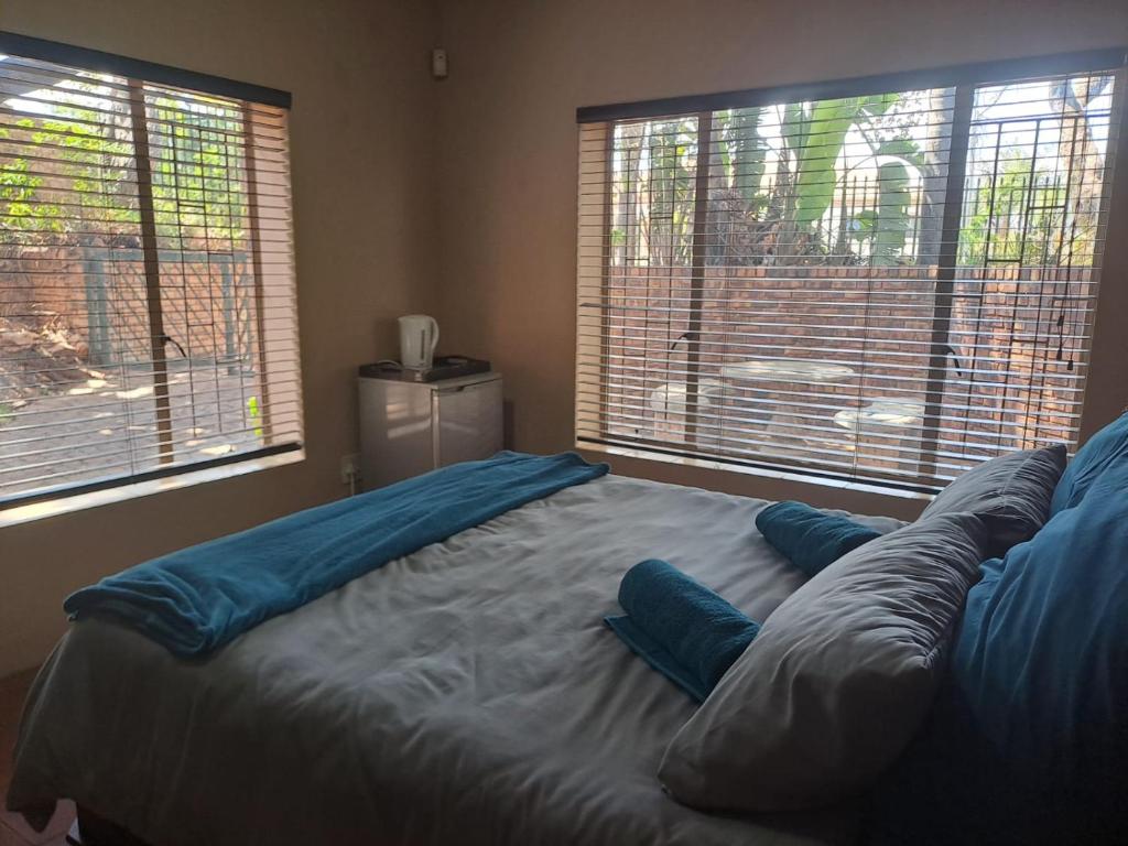 a bed with blue pillows in a room with two windows at Ithiliens Grace Guesthouse in Pretoria