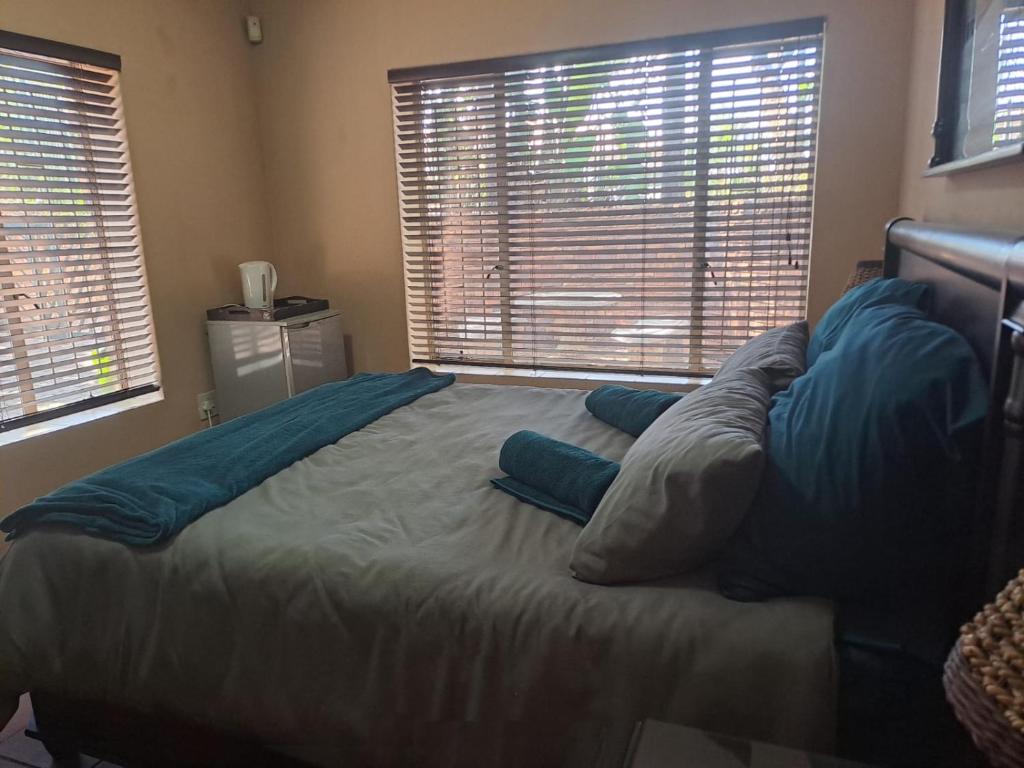 a bedroom with a bed with blue pillows and windows at Ithiliens Grace Guesthouse in Pretoria