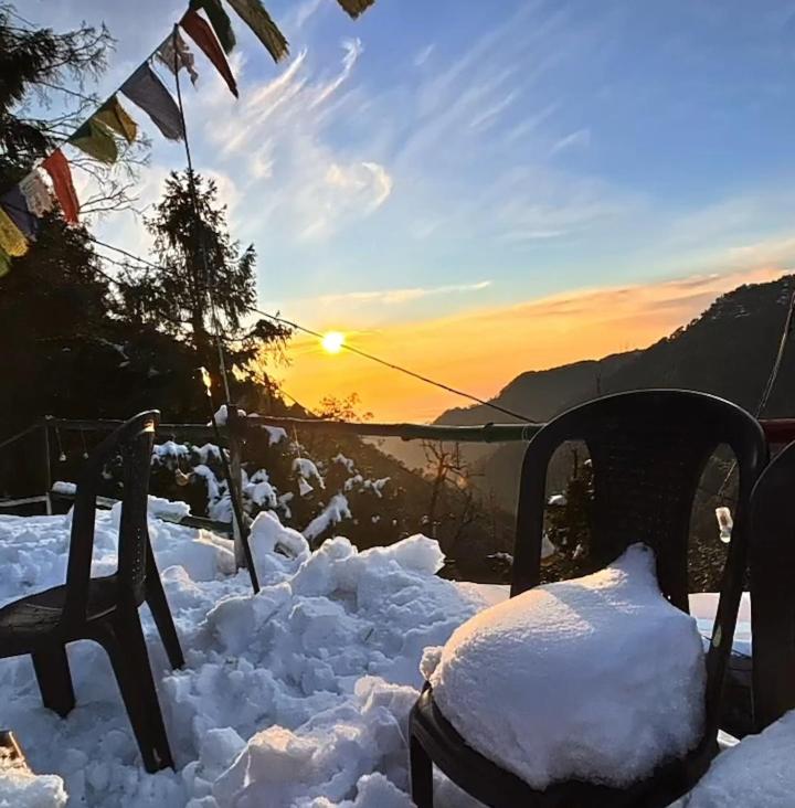 two chairs covered in snow with the sunset in the background at Himalayan Wooden Cottage camping & Cafe Dalhousie in Dalhousie