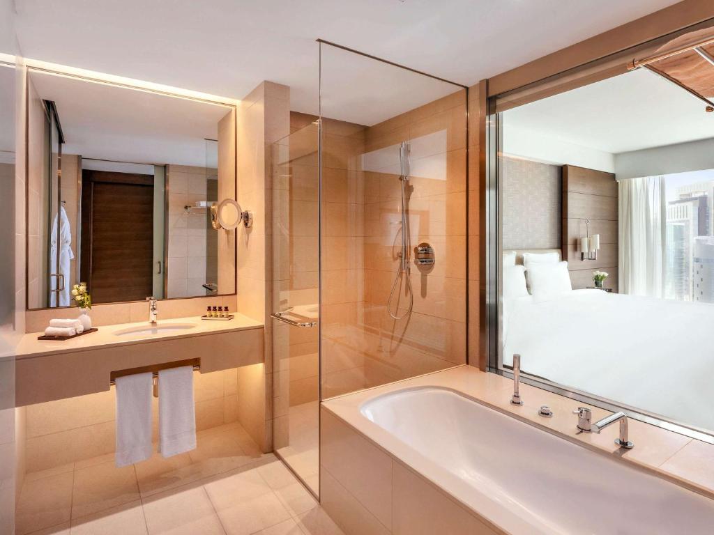 a bathroom with a tub and a shower and a bed at Pullman Doha West Bay in Doha