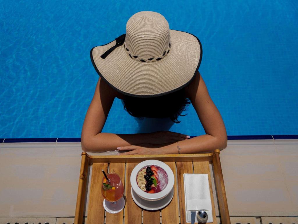 a woman wearing a hat sitting in a table with a bowl of food at Pullman Doha West Bay in Doha