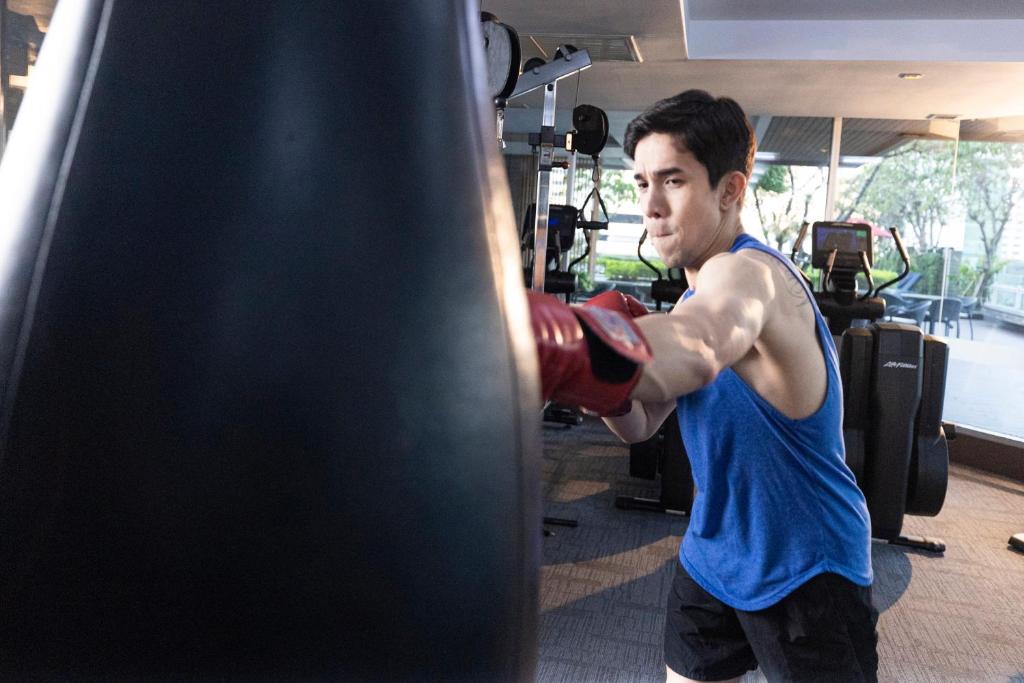A gym scene showing a guest using a freestanding punching bag beside cardio equipment.