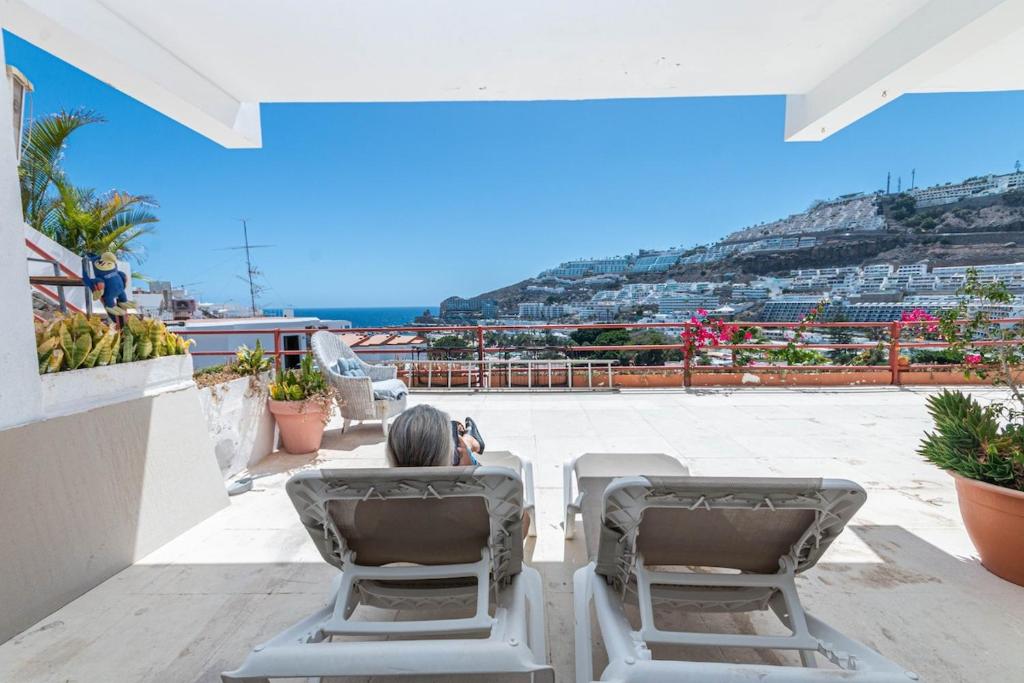 una persona seduta su un balcone con vista e sedie di Sunrise Studio Puerto Rico a Mogán