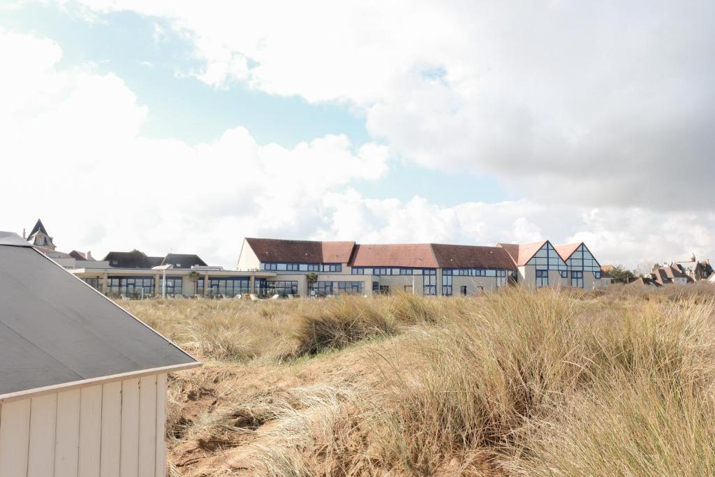 a row of houses on a beach with tall grass at Thalazur Ouistreham - Hôtel & Spa in Ouistreham