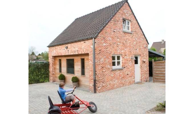 a man sitting on a motorcycle in front of a brick house at De Bosbeekpoort in Oudsbergen 