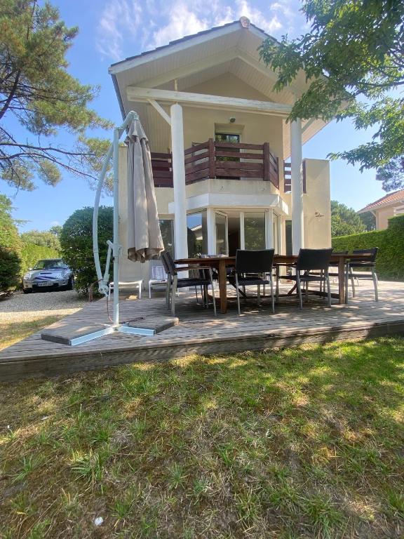 une maison avec une table, des chaises et un parasol dans l'établissement VILLA LACANAU OCÉAN DANS LE GOLF, à Lacanau-Océan