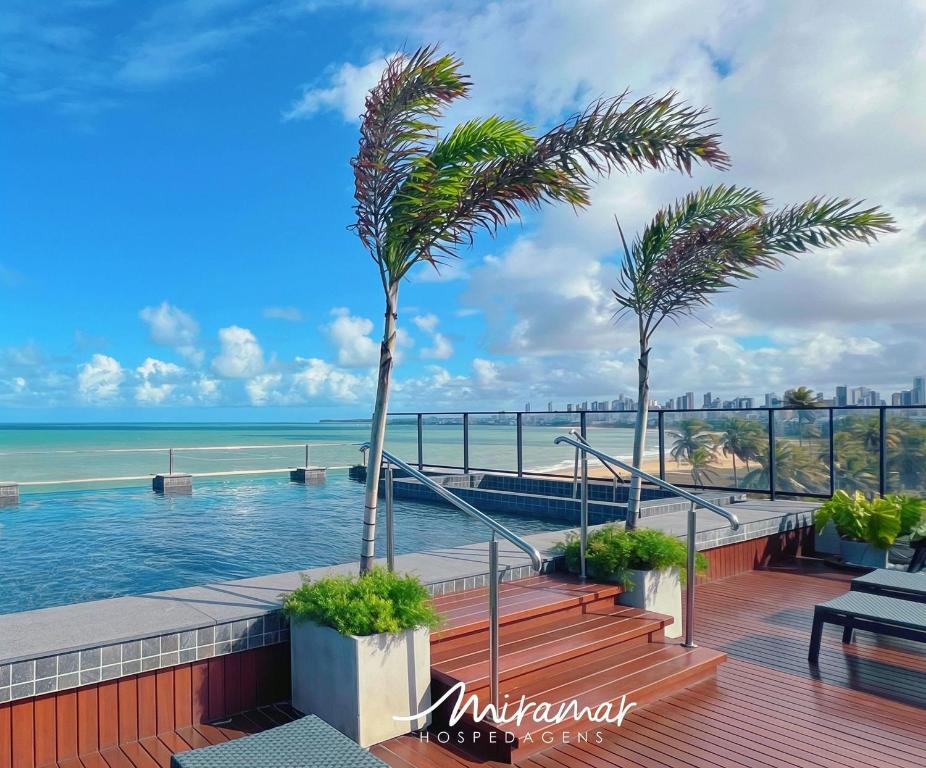 a swimming pool with a palm tree and the ocean at Alta Garden- Pé Na Areia- MH in João Pessoa