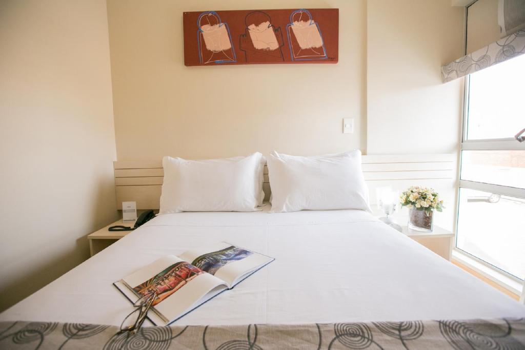 Un dormitorio con una cama blanca con un libro. en Verona Hplus Long Stay, en Brasilia